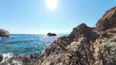 Rocky Cliffs 'in ön planda olduğu sahil sahnesi, dalgalar aşağı düşüyor. Güneş yüksektir ve canlı bir Açı etkisi yaratır. Okyanus ve Kayaları yakalar..