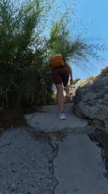 Dikey video. Stone Steps 'e tırmanan bir kadının alçak açılı görüntüsü. Güneş tepede parlıyor. Sırt çantası ve çevre yeşillik Geniş Açı perspektifi tarafından vurgulanır.