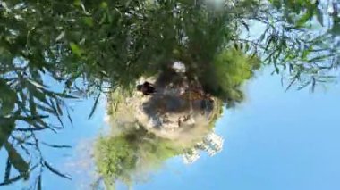 Minik Gezegen etkisi, arka planda okyanus görünen uzun yeşil bitki örtüsüyle çevrili dar bir uçurum kenarında yürüyen bir adam ve kadını gösteriyor..