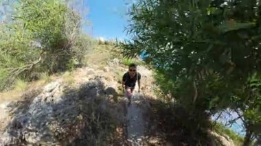 Bir erkek ve kadının geniş açılı görüntüsü okyanusa bakan bir uçurum kenarında yürüyor, güneş parıldıyor ve uzaktaki binalar.