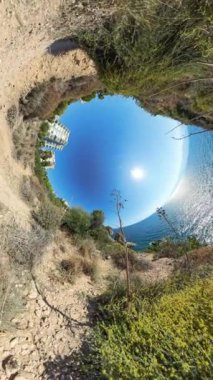 Dikey video. Bir kıyı manzarasının 360. Delik etkisi. Yol ve çevresindeki bitki örtüsü eğrisi merkezde okyanus ve güneş olan dairesel bir manzara yaratıyor..