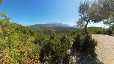 Uçurum boyunca yürüyorum. Bereketli, yeşil bir vadinin geniş açılı görüntüsü. Parlak, berrak bir gökyüzünün altında dağlar var. Sahne, geniş doğal manzarayı panoramik bir manzarayla yakalar..