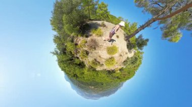 Minik Gezegen etkisi, küçük bir tepedeki bir kadını minyatür küresel bir dünyaya dönüştürür. Parlak mavi gökyüzü, gerçeküstü ve sürükleyici bir görüntü için sahne etrafında kıvrılır..