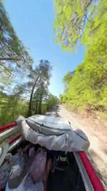 Dikey video. Bir off-road aracının arkasından çekilen 360 derecelik kamera, yolcuları aracın virajlı bir Orman yoluna tırmanırken gösteriyor. Hareket bulanıklığı Araç hareketini vurgular.