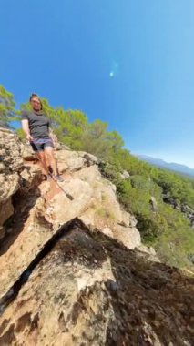 Dikey video. Küçük Gezegen etkisi, etrafındaki kayalar ve ağaçlar etrafında dönerken bir adamın uçurumun kenarında durduğunu gösteriyor. Derin Kanyon ve parlak güneş dramatik manzaraya ekleniyor..