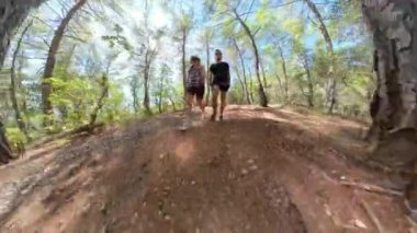 Küçük gezegen. Bir adam ve bir kadın, alçak bir perspektiften yakalanarak orman yolunda yürür. Geniş açı, engebeli araziyi ve parlak güneş ışığı altında yükselen ağaçları vurguluyor..