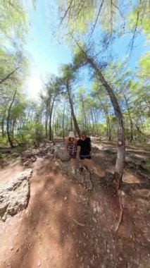 Dikey video. Bir süper geniş açı çekimi ağaçlar orman yolunda yürüyen adam ve kadının etrafındaki kıvrımları bozuyor. Gerçeküstü etki, etrafını saran ormanın dairesel ve sürükleyici bir görüntüsünü yaratıyor..