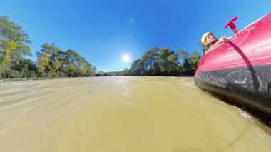 Bir rafting teknesinin yan görüntüsü, parlak güneşin altında geniş açılı bir açıyla küreği tutan kişiyi yakalamak..