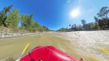 Rafting teknesinin beyaz su akıntılarından geçerken, kameraya doğru akan su ve arka planda parlayan güneş ışığıyla ön cephede çekilmiş görüntüsü..