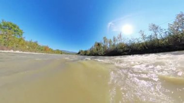 Nehrin geniş açılı bir görüntüsü doğal bir manzara boyunca akar, güneş ışığı su ve nehir kıyısındaki ağaçlardan yansıyarak akıntının hareketini yakalar..