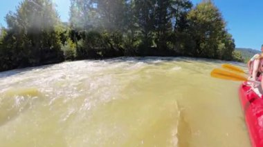 Rafting macerası sırasında hızlı akan bir nehre yakın, salın kenarı ve kürekleri görünür, yoğun yeşil ağaçlar ve parlak güneşli gökyüzünün altında dağlarla çevrili..