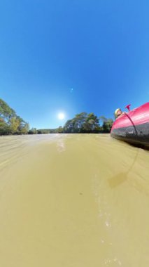 Dikey video. Bir rafting teknesinin yan görüntüsü, parlak güneşin altında geniş açılı bir açıyla küreği tutan kişiyi yakalamak..