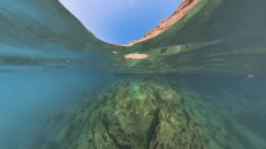 Suyun yüzeyindeki kayalık kayalıkların yansımasını yansıtan barışçıl bir sualtı görüntüsü, sualtı manzarasını gösteren turkuaz bir su..