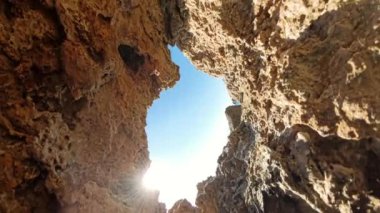 360 derece dönüş. Düşük açılı bir manzara, güneş ışığı içinden geçerken yukarıdaki parlak gökyüzü ile kayalık dokusu arasında çarpıcı bir kontrastlık yaratır..