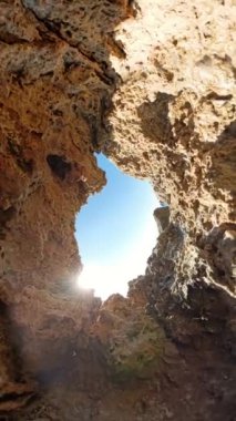 Dikey video. 360 derece dönüş. Düşük açılı bir manzara, güneş ışığı içinden geçerken yukarıdaki parlak gökyüzü ile kayalık dokusu arasında çarpıcı bir kontrastlık yaratır..