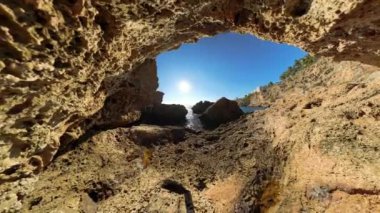 Yakınlaşın, kayalık bir mağaranın içinden bir manzara büyüleyici bir deniz manzarası sergiliyor, güneş okyanusun üzerinde parlıyor ve engebeli kayalıklar mağaranın girişi tarafından çerçeveleniyor..