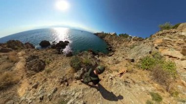 Güneşin denizin üzerinde parladığı kayalık bir sahil yolundan inen yürüyüşçülerin tepeden aşağı bakışı. Dik kayalıklar ve okyanus ufku dinamik ve maceralı bir sahne yaratır..