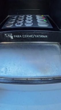Dikey video. ATM 'den para çeken bir elin yakın plan çekimi, birinci şahıs perspektifi sağlıyor, para transferi sırasında makineyle etkileşime odaklanıyor.