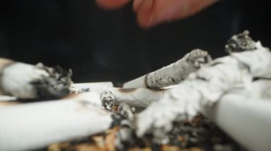 A close-up of a hand extinguishing a cigarette butt in a pile of ashes, with smoke rising from the remnants. The detailed view highlights the act of putting out the cigarette.