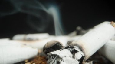 A discarded cigarette butt lies smoldering on a surface surrounded by ashes, while the camera moves backward, creating a dynamic effect that reveals the scene of smoking waste.