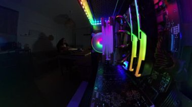 Oyun bilgisayarının içinden 360 derecelik bir görüntü masasında oturan, loş ışıklı bir odada çip yiyen, renkli RGB ışıkları ve bilgisayar parçalarıyla çevrili çıplak bir adamı gösteriyor..