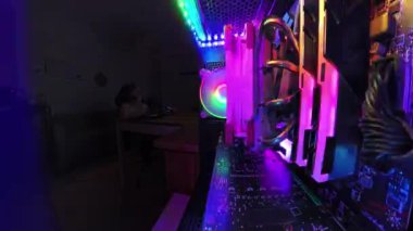 Geniş açılı, yakın plan bir oyun bilgisayarının içinde parlayan RGB aydınlatma ve soğutma vantilatörleri ile, bir zaman atlaması, loş ışıklı bir odada masasında otururken üstsüz bir adamın cips yemesini yakalıyor..