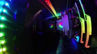 Bir adamın cam paneli kumaşla silerken canlı RGB ışıklandırma ve donanım bileşenlerini gösteren bir oyun bilgisayarının içinden yakından görüntü. Aydınlatılmış bileşenler ve renkli ışıklar yüksek teknolojili, temiz bir atmosfer yaratıyor..