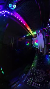 Dikey video. Bir adamın cam paneli kumaşla silerken canlı RGB ışıklandırma ve donanım bileşenlerini gösteren bir oyun bilgisayarının içinden yakından görüntü. Aydınlatılmış bileşenler ve renkli ışıklar yüksek teknolojili, temiz bir atmosfer yaratıyor..