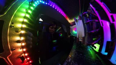 Kamera geri çekilirken, bir adam oyun bilgisayarının cam yan panelini kapatıyor, canlı RGB aydınlatma ve donanım bileşenlerini geniş açılı, büyüleyici bir bakış açısıyla gösteriyor. Aydınlatılmış iç mekan, yüksek teknoloji kurulumunu vurguluyor..