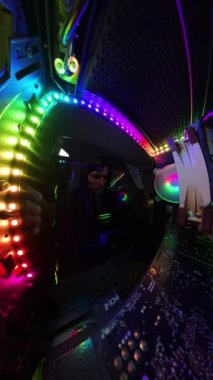Dikey video. Kamera geri çekilirken, bir adam oyun bilgisayarının cam yan panelini kapatıyor, canlı RGB aydınlatma ve donanım bileşenlerini geniş açılı, büyüleyici bir bakış açısıyla gösteriyor. Aydınlatılmış iç mekan, yüksek teknoloji kurulumunu vurguluyor..