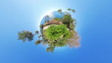 Geniş açılı Minik Gezegen efekti yeşil, ağaçlar ve okyanusla dolu küçük dairesel bir dünya yakalar, berrak mavi bir gökyüzü, dingin ve canlı bir manzara yaratır..