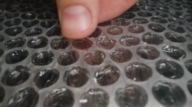 Baloncuk ambalajına bastırılmış parmakları yakın plan, koruyucu hava kabarcıklarını patlatmak, detaylı, tatmin edici bir hareketle dokulu plastik yüzey ile dokunsal etkileşimi göstermek.