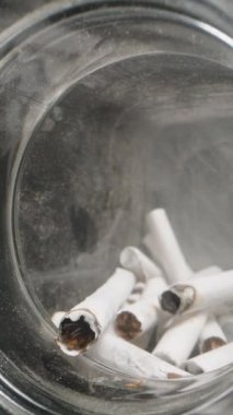 Dikey video. Sigara izmaritleriyle dolu bir cam kavanozun içinde hareket eden Dolly sürgülü fotoğraf, küllerin dokusunu yakalıyor ve sınırlı, kumlu bir alanda kullanılan filtreleri yakalıyor, atıkları ve atıkları vurguluyor.