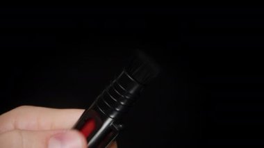 Geri çekilebilir kamera temizleme fırçasının, mekanizmasını göstermek için fırçayı tutan bir elle gösterimi, koyu arkaplana karşı kompakt tasarım ve işlevselliği vurguluyor.
