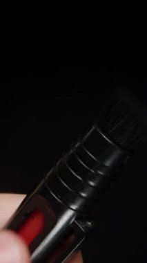Dikey video. Geri çekilebilir kamera temizleme fırçasının, mekanizmasını göstermek için fırçayı tutan bir elle gösterimi, koyu arkaplana karşı kompakt tasarım ve işlevselliği vurguluyor.