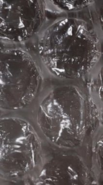 Dikey video. Hava boşluklarını gösteren baloncuk ambalajının yakın plan görüntüleri, ambalaj malzemesinin şeffaflığını ve koruyucu doğasını vurgulayarak, ışık altında parlak bir bitiriş ile.