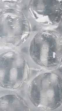 Dikey video. Işığın altında baloncuk ambalajının makro çekimi, şişirilmiş hava hücrelerini ve temiz plastik yapısını vurgulamak, yumuşak, esnek bir tasarımla kırılgan maddeleri yastık altına almak ve korumak için mükemmel..