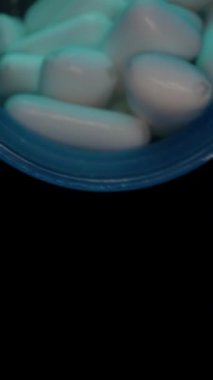 Dikey video. Bir el mavi bir sakız kutusundan beyaz sakız tabletlerini düşük ışık ayarlı bir avuç içine döker, tazelik, doku ve yavaş çekimde kullanımı üzerine odaklanır..