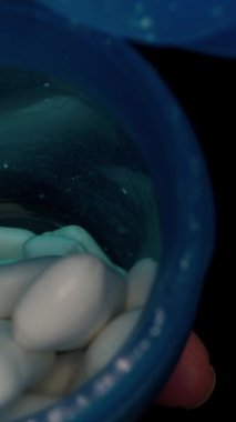 Dikey video. Bir el mavi bir sakız kutusundan beyaz sakız tabletlerini düşük ışık ayarlı bir avuç içine döker, tazelik, doku ve yavaş çekimde kullanımı üzerine odaklanır..