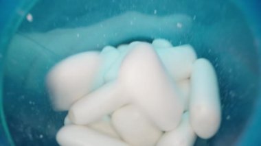 Bulanık, dinamik bir hareketle mavi bir kabın içine dökülen beyaz nane sakızı tabletlerinin yakın plan çekimi canlı bir sahnede tazeliği ve yumuşak, pürüzsüz dokuyu vurguluyor..