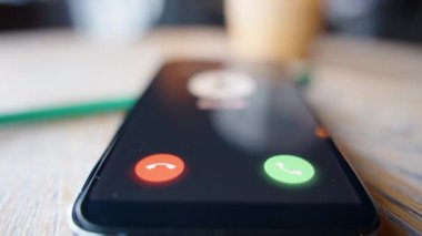 Tahta bir masanın üzerindeki akıllı telefonun düşük açılı yakın plan görüntüsü, gelen bir dümen çağrısını gösteriyor, dikkat ve dijital tehdit bilinci temasını vurguluyor.