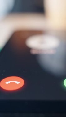 Dikey video. Tahta bir masanın üzerindeki akıllı telefonun düşük açılı yakın plan görüntüsü, gelen bir dümen çağrısını gösteriyor, dikkat ve dijital tehdit bilinci temasını vurguluyor.