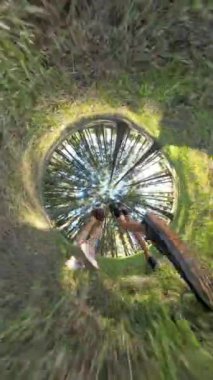 Dikey video. Aşağıdan küresel panoramik bir manzara, yemyeşil bir ormanda yürüyen bir erkek ve kadını yakalar ve küçük gezegen etkisiyle manzaraya dinamik bir bükülme katar..