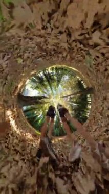 Dikey video. Bir adam ve bir kadın düşen yapraklardan oluşan tünel gibi bir çerçevede yürür, kamera onları aşağıdan yakalar, canlı sonbahar renkleriyle çevrili sürrealist bir manzara yaratır..