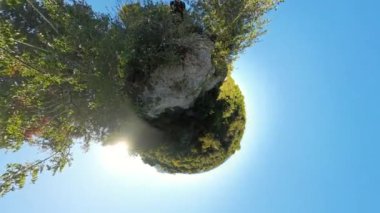 Yüksek ağaçlar ve açık mavi gökyüzü ile yemyeşil bitki örtüsünden oluşan küçük bir gezegen manzarası küresel bir manzara oluşturuyor. Parlak güneş ışığı sahnenin etrafına ışık saçar..