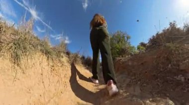 Toprak yolda yürüyen bir kadının dinamik hareketi ve yolu çevreleyen doğal bitkileri yakaladığı düşük açılı görüntüsü.