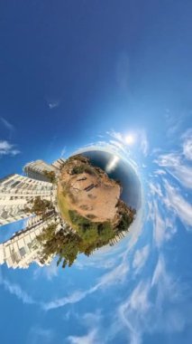 Dikey video. Denize bakan bir uçurumun kenarında duran bir kadın ve erkeğin küçük bir gezegen etkisi görüntüsü. Arka planda uzak dağlar ve derinliği arttıran yakınlaştırılmış bir perspektif..