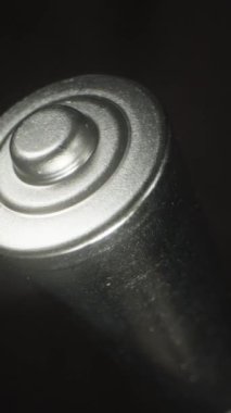 Dikey video. Siyah arkaplana karşı dönen metalik bataryanın yakın plan görüntüsü silindirik gövdeye ve desenli kapağa odaklanıyor. Çekimde endüstriyel tasarım ve metalik kaplama vurgulandı.