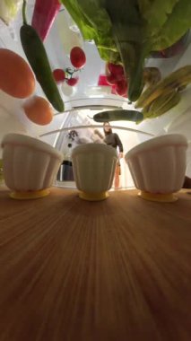 Buzdolabının içinden bir adamın kapıyı açtığını ve bir fincan jöleye uzandığını görmek. Balık gözü perspektifi çeşitli yiyecekler ve ön planda ahşap bir raf yakalar..