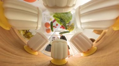 Buzdolabının içinden geniş açılı, kıvrımlı bir bakış açısı olan bir adam jöle kabını tutmak için uzanır. Atış, ahşap bir rafta sıralanmış yiyeceklerin çeşitliliğini vurguluyor..